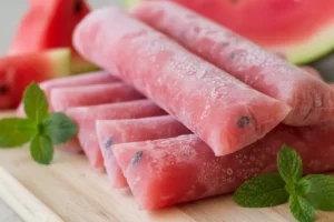 Geladinho de melancia vermelho vibrante em saquinho transparente, com sementes visíveis e gotas de água, sobremesa gelada de verão.